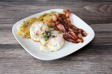 A view of a breakfast plate, featuring eggs over easy, bacon and shredded hash browns.