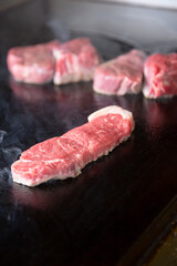 A view of some raw beef cooking on a restaurant griddle surface.