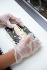 A view of hands preparing a sushi roll at an ingredient station.