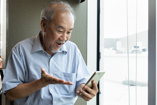 Excited happy smiling old asian senior man using smartphone with joy