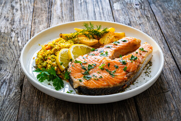 Fried salmon steak with French fries and fresh vegetable salad served on wooden table
