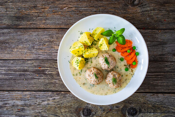 Boiled meatballs in dill sauce with potato puree, carrots and peas on wooden table
