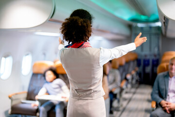 Air hostess or airline staff woman demostrate and guide the emergency exit of airplane to the...