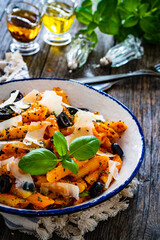 Noodles with pesto, parmesan cheese, basil and black olives served on wooden table