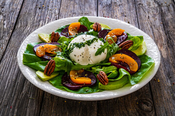 Burrata cheese with roasted beets, greens, peaches and pecan nuts on wooden table
