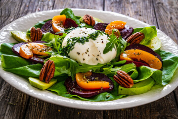 Burrata cheese with roasted beets, greens, peaches and pecan nuts on wooden table
