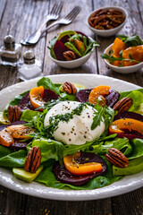 Burrata cheese with roasted beets, greens, peaches and pecan nuts on wooden table
