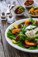 Burrata cheese with roasted beets, greens, peaches and pecan nuts on wooden table
