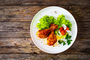 Barbecue chicken drumsticks with lettuce and tomatoes on wooden table
