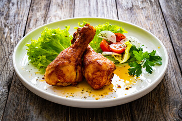 Barbecue chicken drumsticks with lettuce and tomatoes on wooden table
