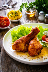 Barbecue chicken drumsticks with lettuce and tomatoes on wooden table

