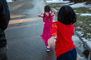 two small children march happily down snowy street with their parent