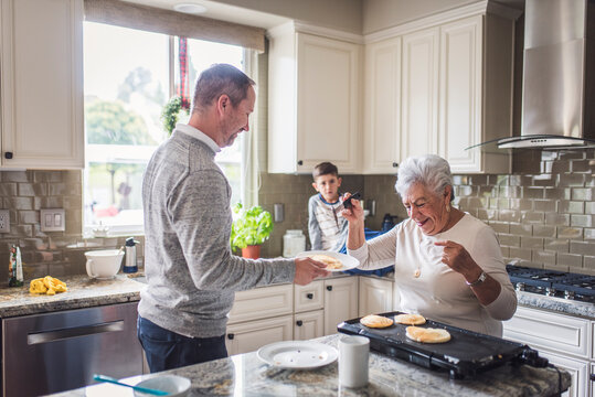 Senior woman serving pancakes to her adult grandson and greatgrandson