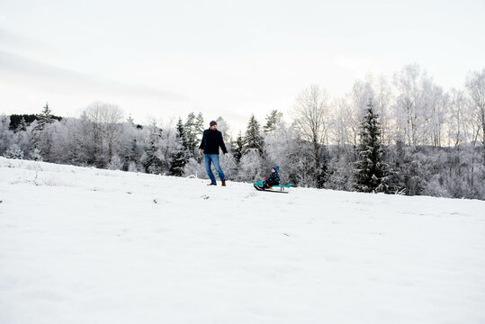 Father son walking sledging in snow white forest winter wonderland