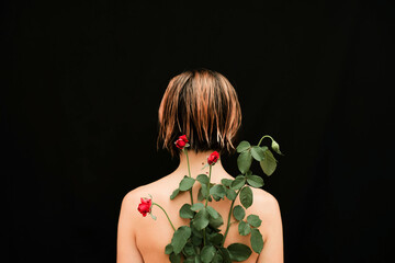 Naked woman with red roses on her back against black background