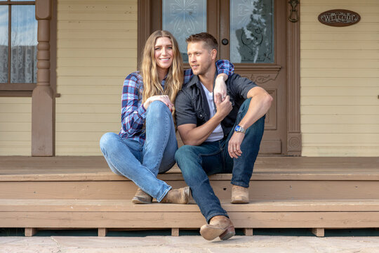Western wear young couple sitting on front porch of ranch house