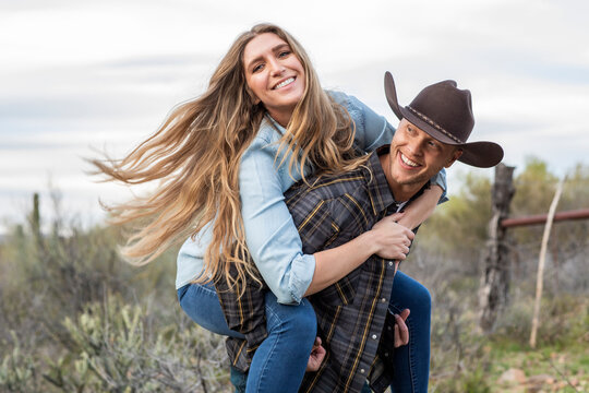 Western wear young couple giving piggy back ride on ranch