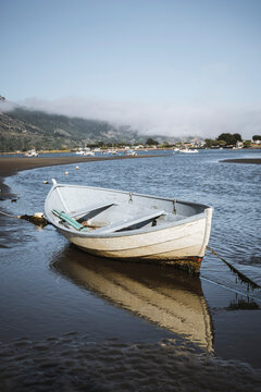 Empty tied up row boat sits on sand at low tide in Bolinas, California