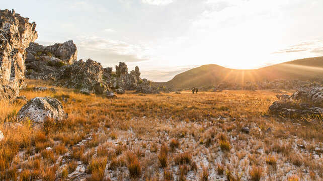 Three hikers walk towards the setting sun in the landscape of Zimbabwe