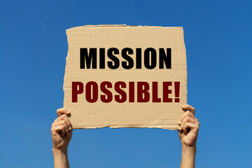 Mission possible on box paper held by 2 hands with isolated blue sky background. This message board...