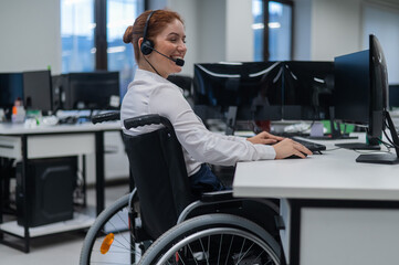 Red-haired caucasian woman in a wheelchair talking on a headset. Female call center worker smiling.
