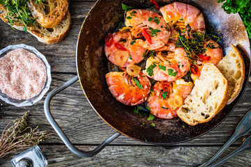 Fried prawns with thyme in cooking pan on wooden table
