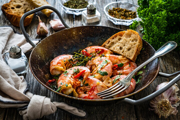 Fried prawns with thyme in cooking pan on wooden table
