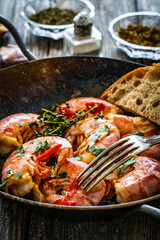 Fried prawns with thyme in cooking pan on wooden table

