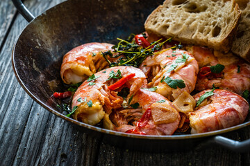 Fried prawns with thyme in cooking pan on wooden table
