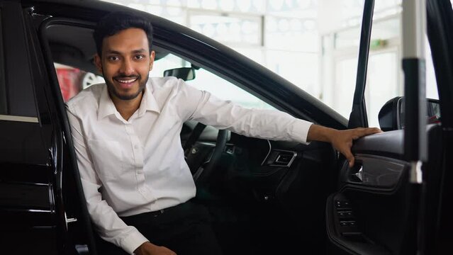 Happy successful indian man sitting in his new electric car in auto showroom. Right hand drive car