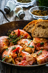 Fried prawns with thyme in cooking pan on wooden table
