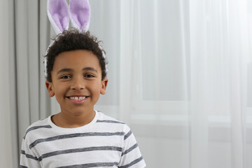 Cute African American boy with Easter bunny ears headband indoors, space for text