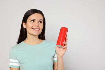 Beautiful young woman holding red tin can with beverage on light grey background. Space for text