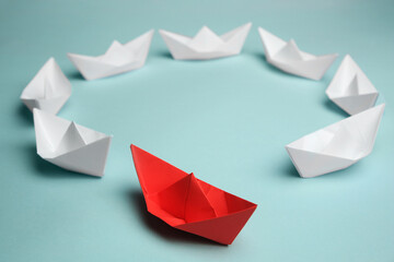 Group of paper boats following red one on light background. Leadership concept