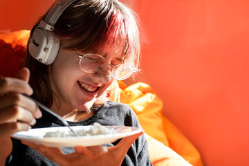 funny teneyger girl with pink hair and glasses eats rice. cozy house