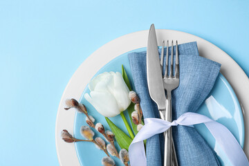 Festive table setting with willow twigs and tulip on light blue background, top view with space for...