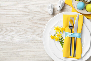 Festive table setting with painted eggs and cutlery on white wooden background, flat lay with space...