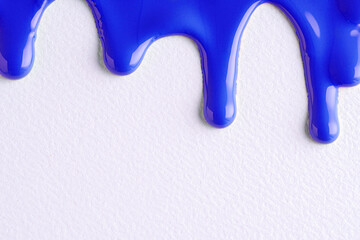 Blue liquid drops of paint color flow down on white canvas. Abstract art. Blue paint dripping on the white wall with copy space.