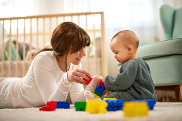 Mother and her baby boy playing with colored toy blocks at home