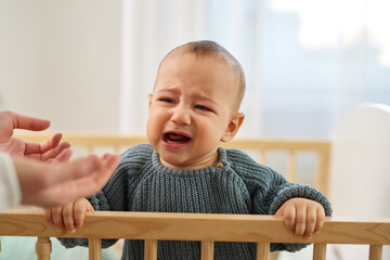Little baby boy crying in the crib while his mother trying to calm him