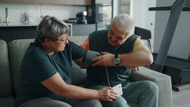 Aged Man Putting Blood Pressure Cuff On Arm Of His Elderly Wife, Using Modern Sphygmomanometer