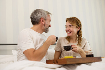 Mature couple enjoying coffee and breakfast in bed