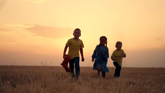 Happy family in nature. Sunset over a wheat field. Children run around the park. Happy family concept. Children play with a teddy bear. Son and daughters walk in wheat field. Family picnic in the park
