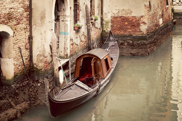 An old gondola on a Venice canal moored to a narrow street exit (vintage style photo)