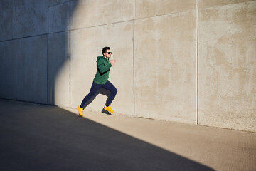 Male runner sprinting during sunny afternoon in the city next to concrete wall. Healthy lifestyle concept