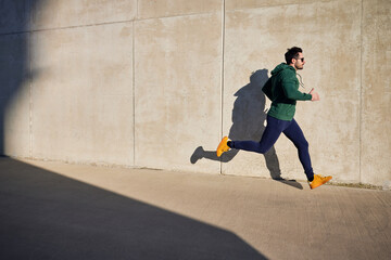 Man running during sunny afternoon in the city next to concrete wall. Active lifestyle concept