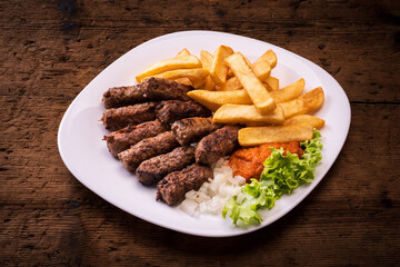 Traditional cevapcici served with sauce and onion french fries. on wooden table