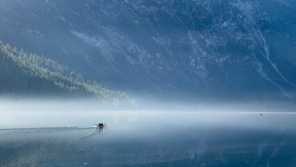 lonely boat drives in the morning haze from the idyllic lake plansee in tyrolean autumn