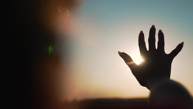 Happy girl pulls her hand towards the sunlight. Silhouette of man in natural park. Girl stretches her hand to the sky. Sun rays through fingers. Woman stretches her hand to sky in nature park