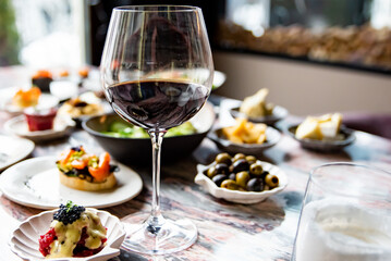 glass with red wine and wine snack set, food from spain, cheese, meat, vegetables and other appetizers on table